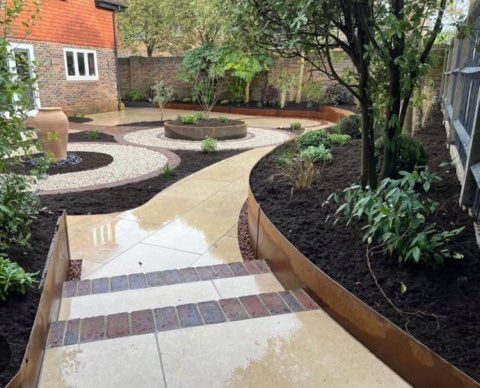 Stone path leads through a landscaped garden with brick stairs, beds, and a terracotta pot.