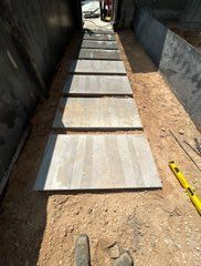 Gray rectangular stepping stones laid in a dirt path between concrete walls; a level and tools are nearby.