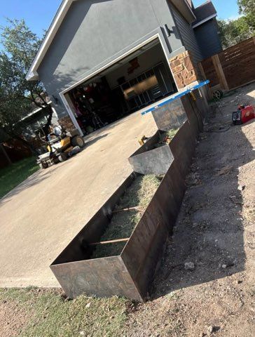 Metal planters under construction next to a driveway and a garage.