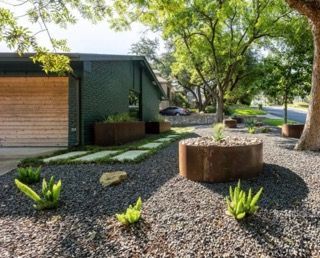 Modern home exterior with gravel landscaping, metal planters, and green plants.