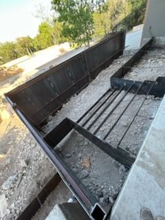 Metal railing frame under construction, partially installed on concrete and gravel.