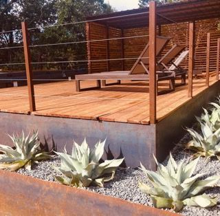 Wooden deck with lounge chairs, surrounded by steel planters with agave plants.