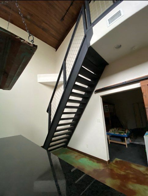 Black metal staircase with wire mesh railing, leading to a loft.