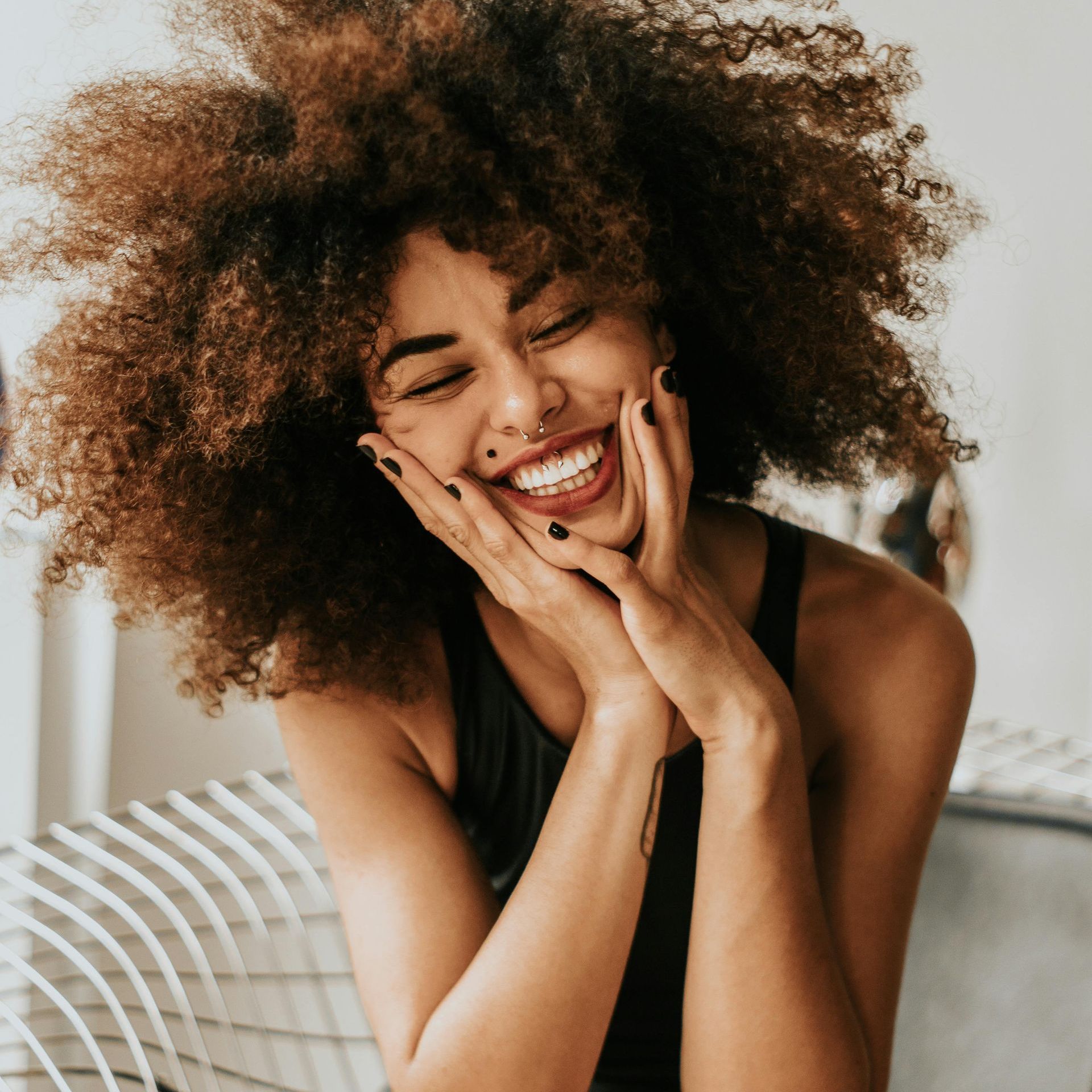 A woman with curly hair is smiling with her hands on her face.