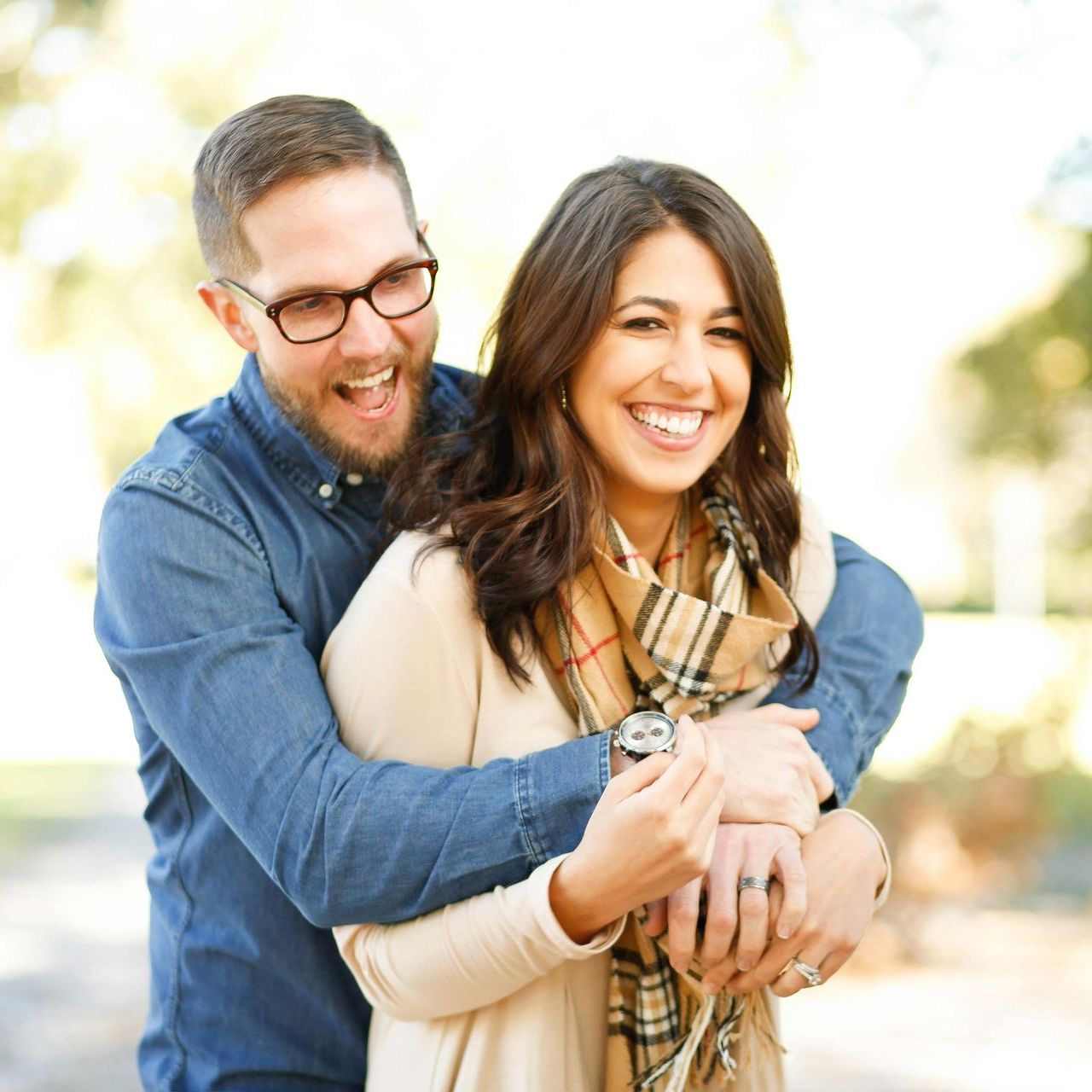A man in glasses is hugging a woman in a plaid scarf