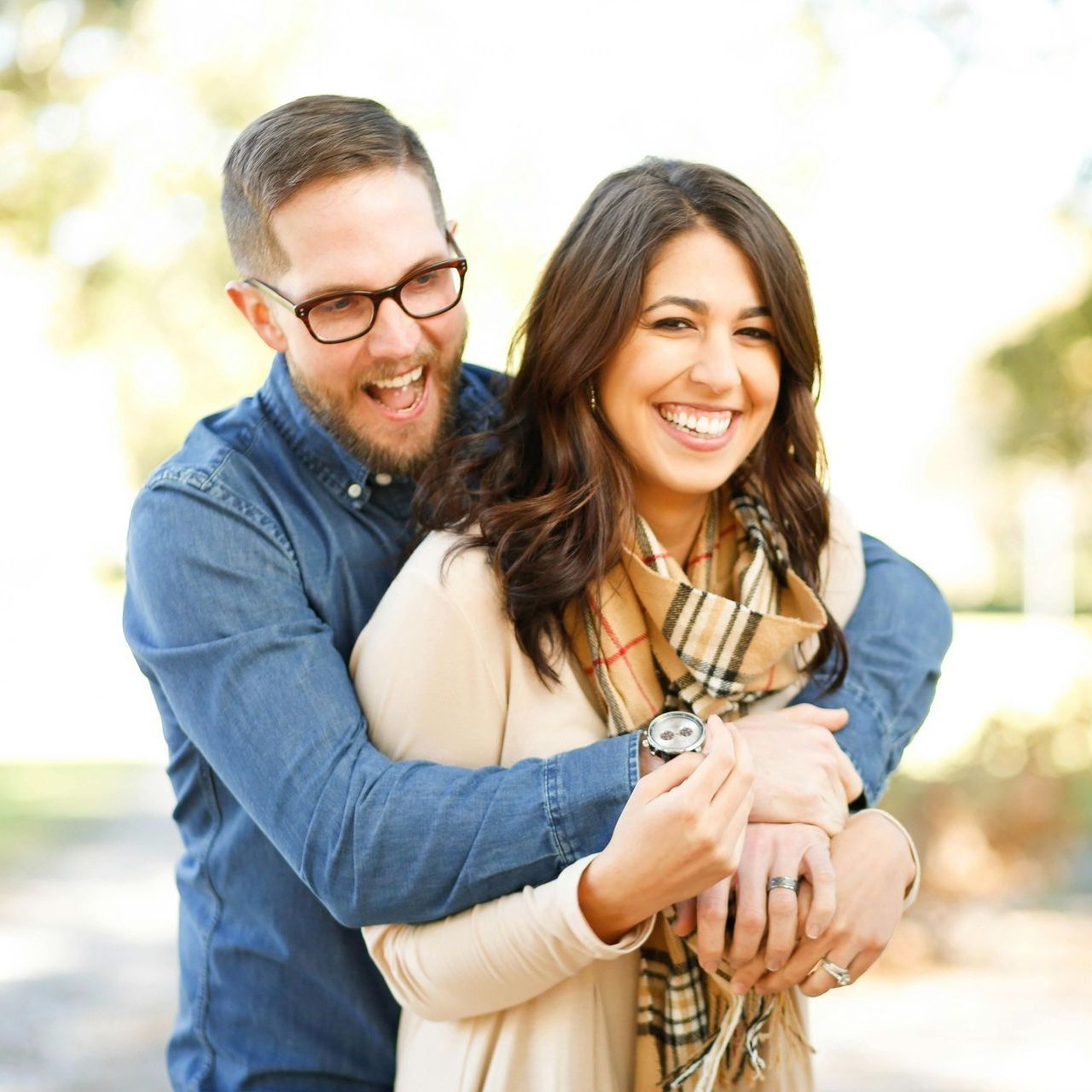A man in glasses is hugging a woman in a plaid scarf