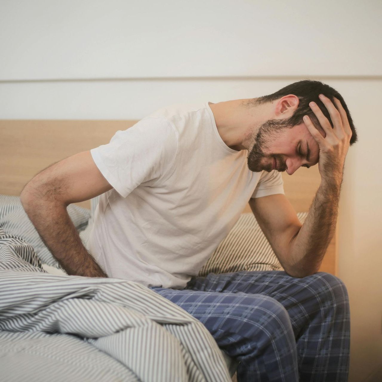 A man is sitting on a bed with his hand on his head.