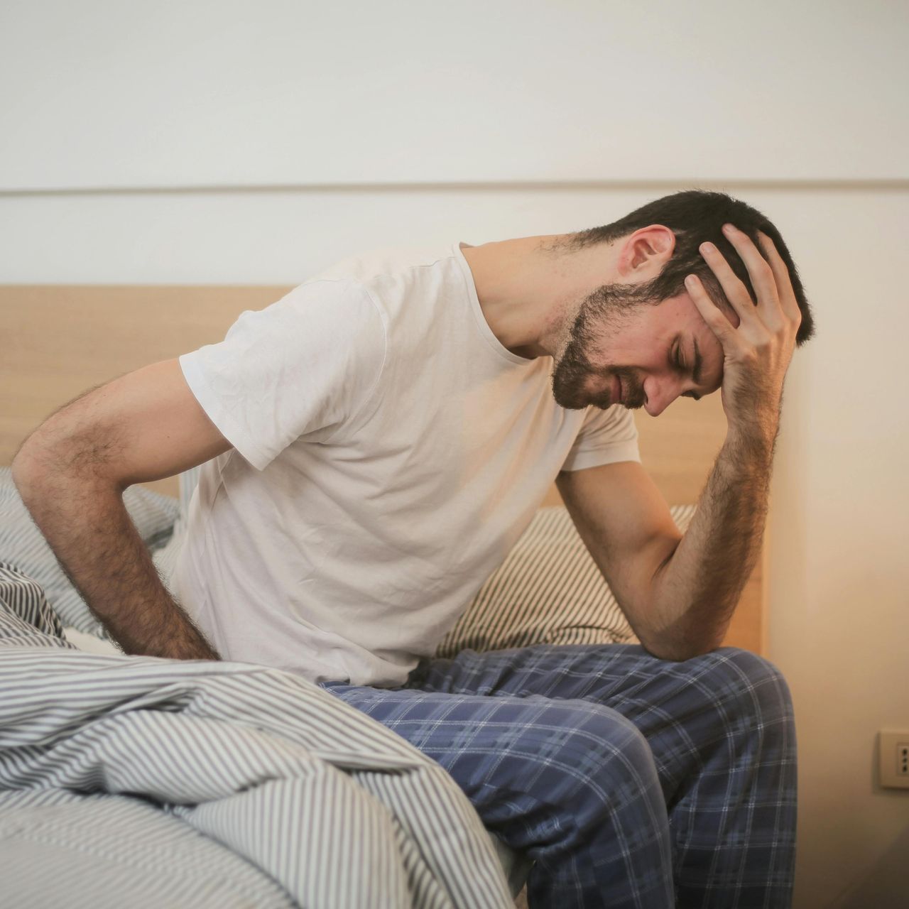 A man is sitting on a bed with his hand on his head.