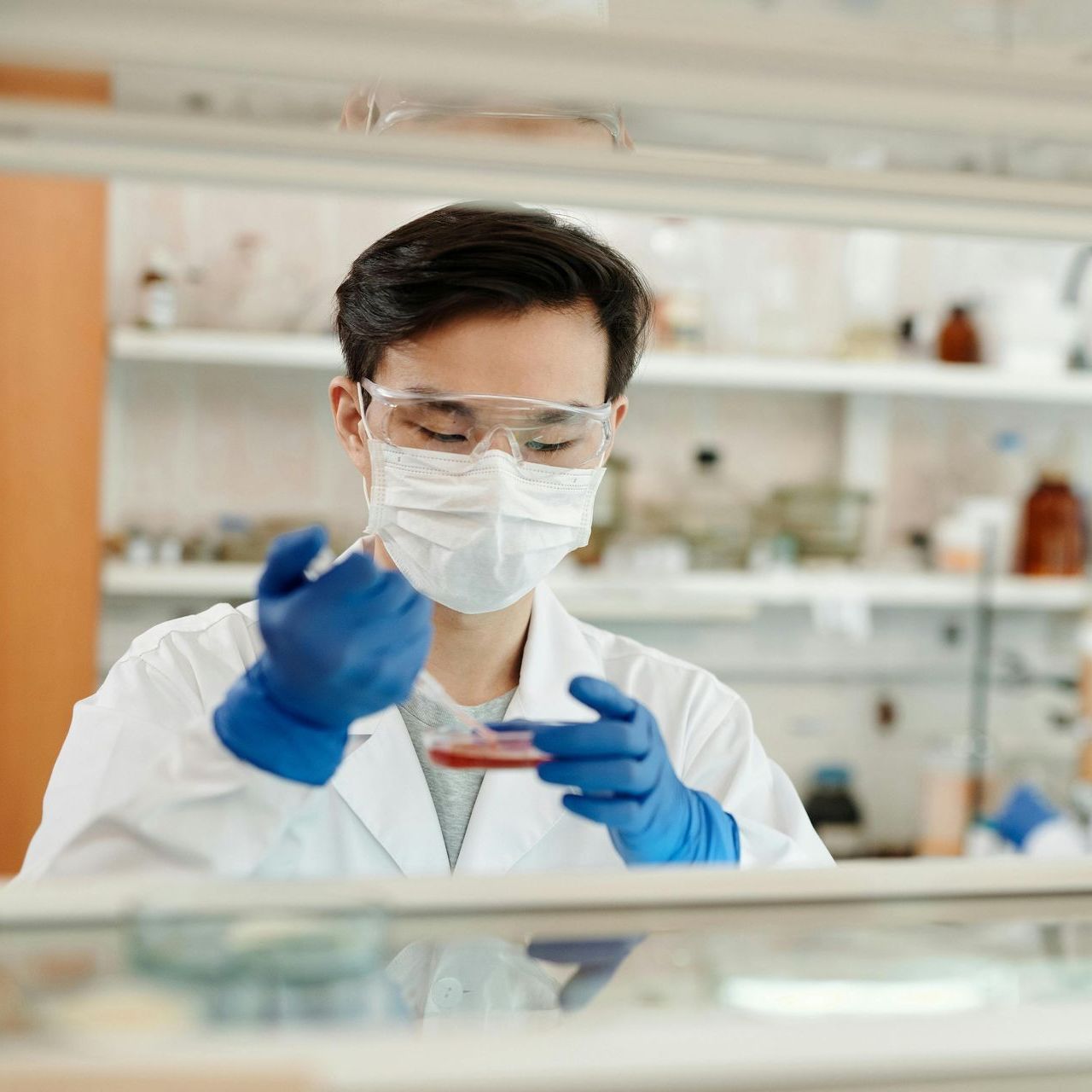 A man wearing a mask and blue gloves is working in a lab.