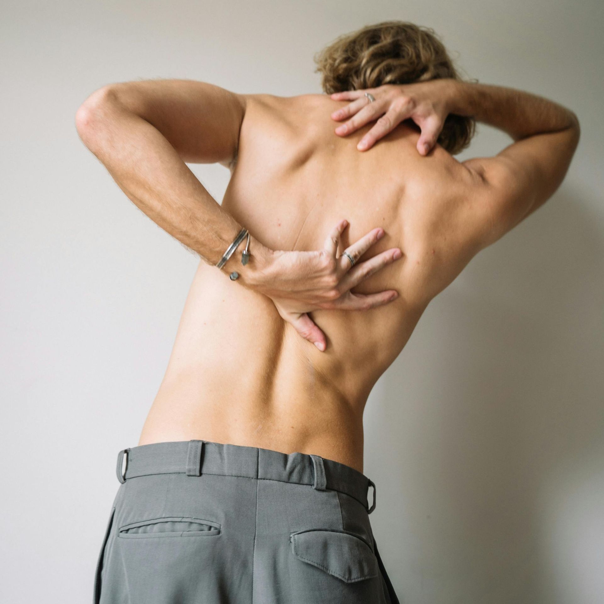 A shirtless man is holding his back in pain