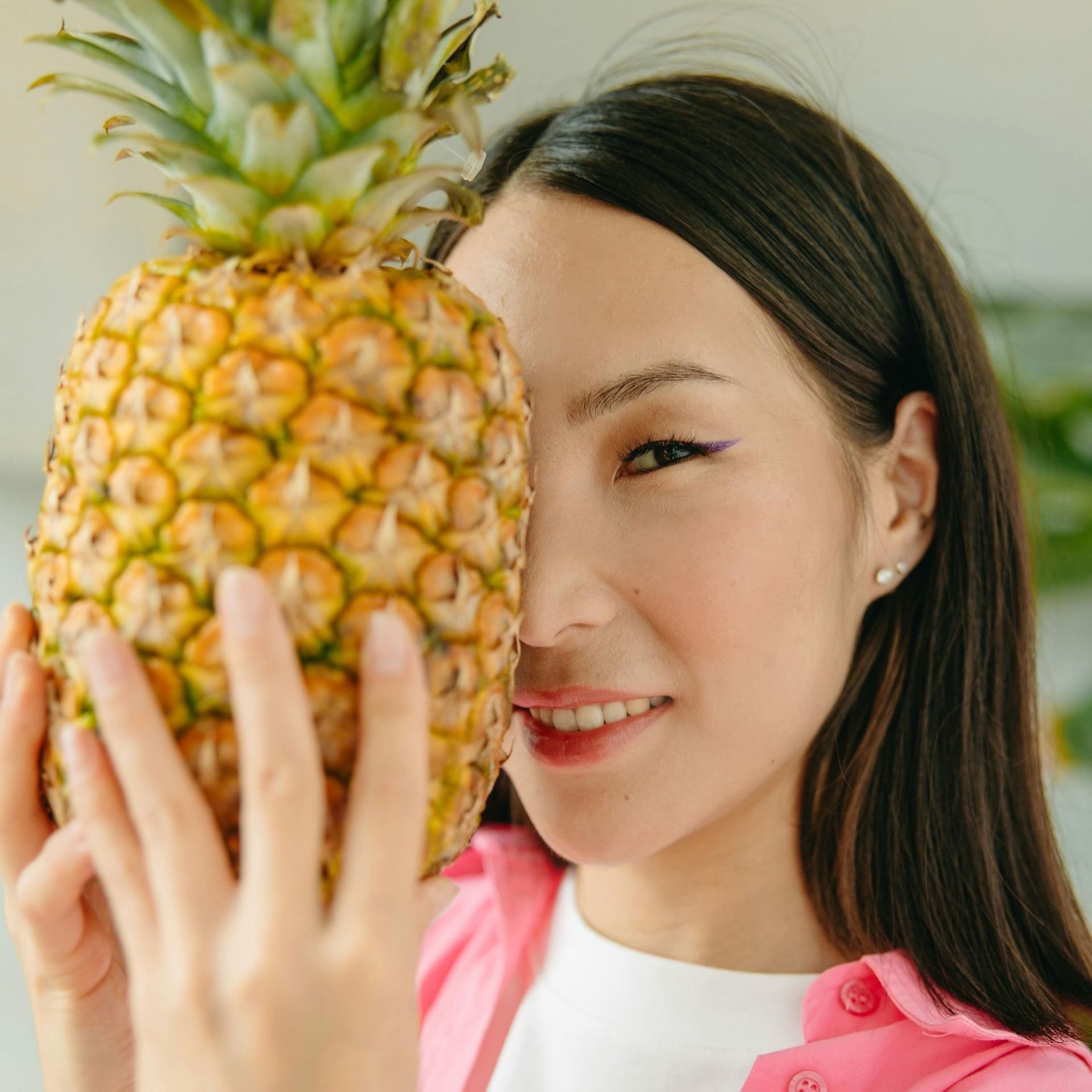 A woman is holding a pineapple in front of her face