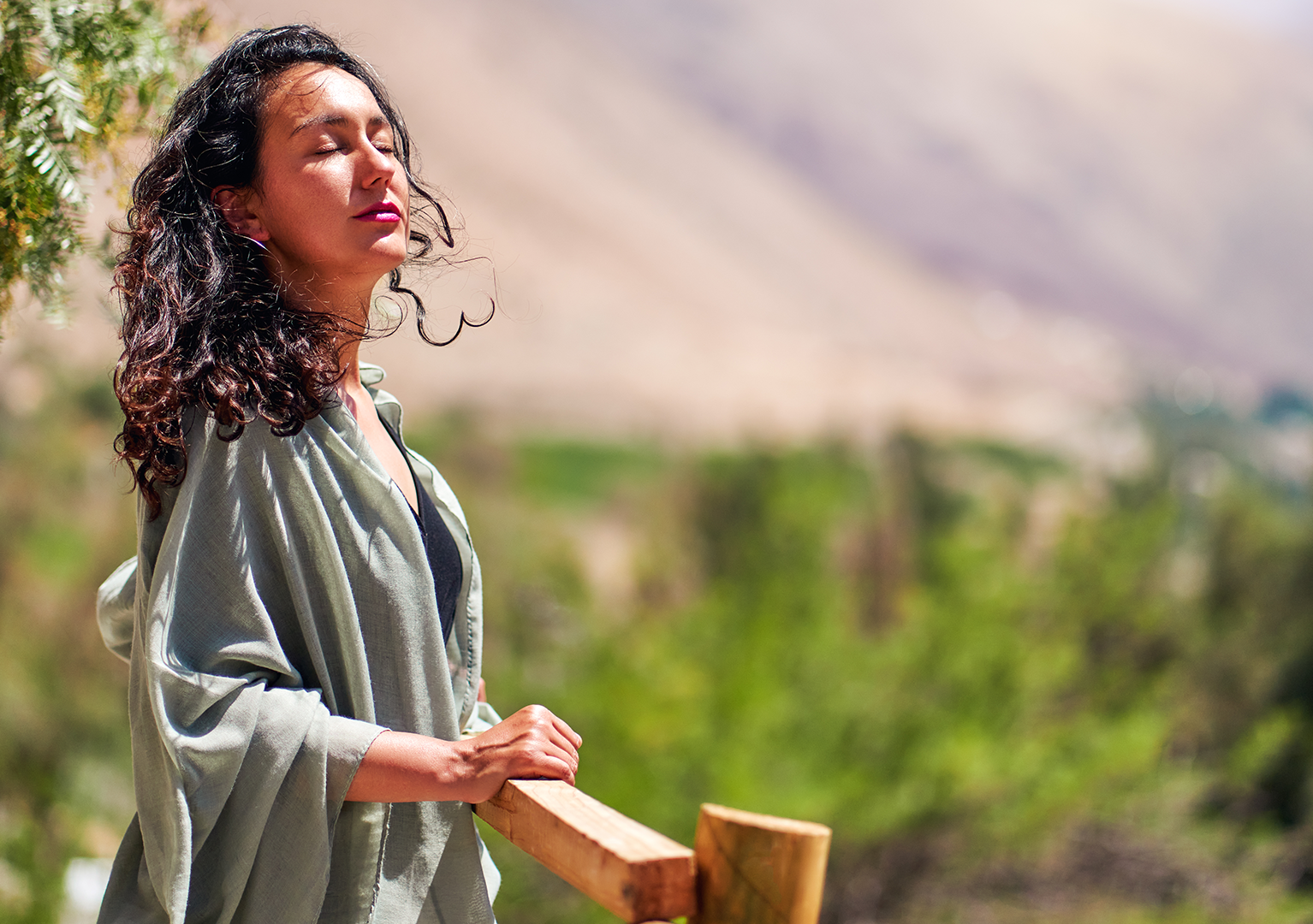 A woman is standing on a wooden railing with her eyes closed.