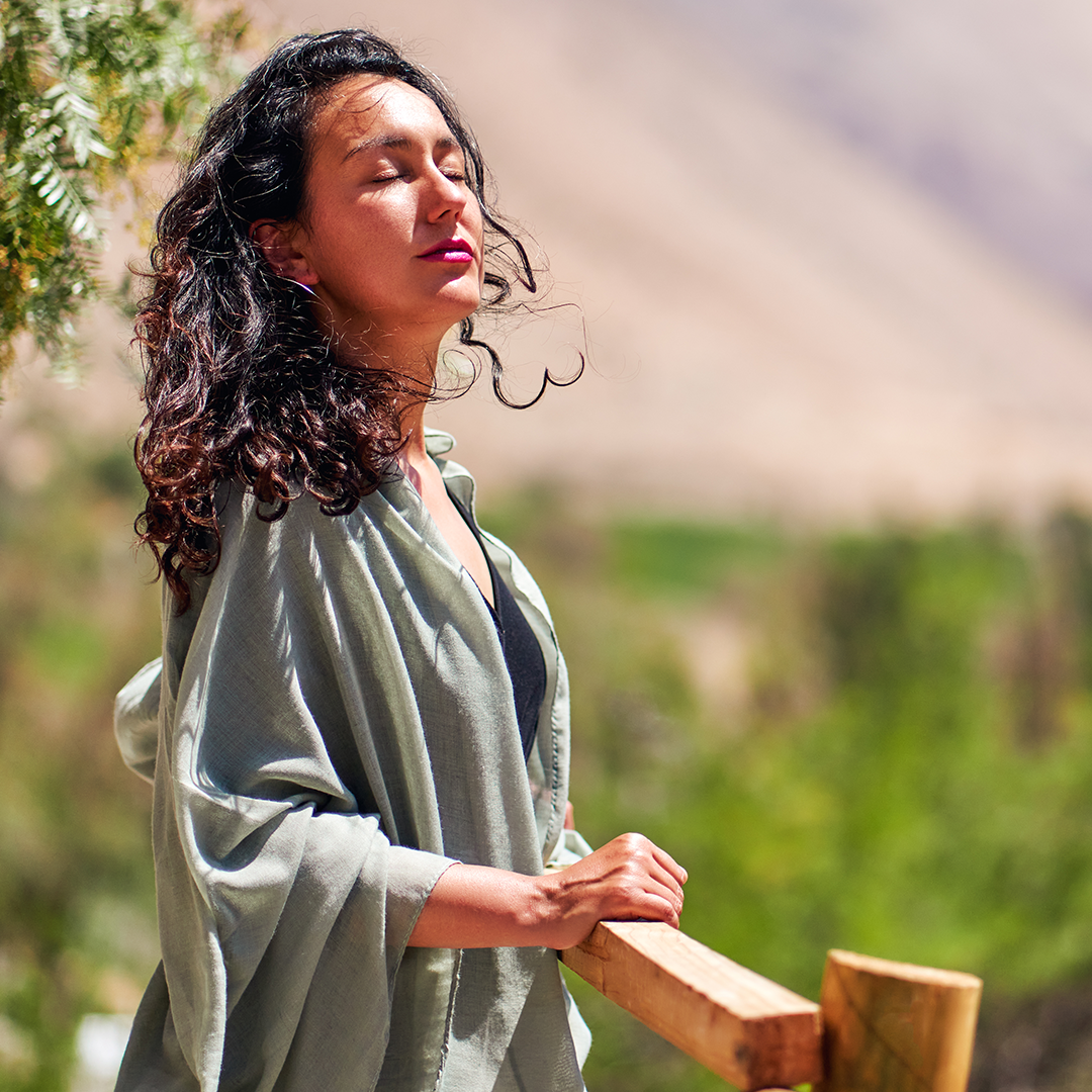 A woman is standing on a wooden railing with her eyes closed