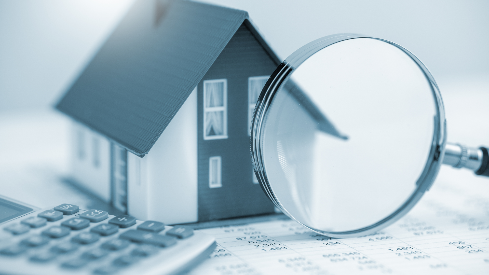 A magnifying glass is sitting next to a model house and a calculator.