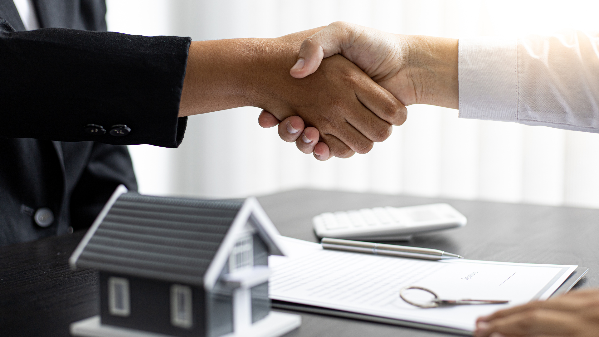 A man and a woman are shaking hands in front of a model house.