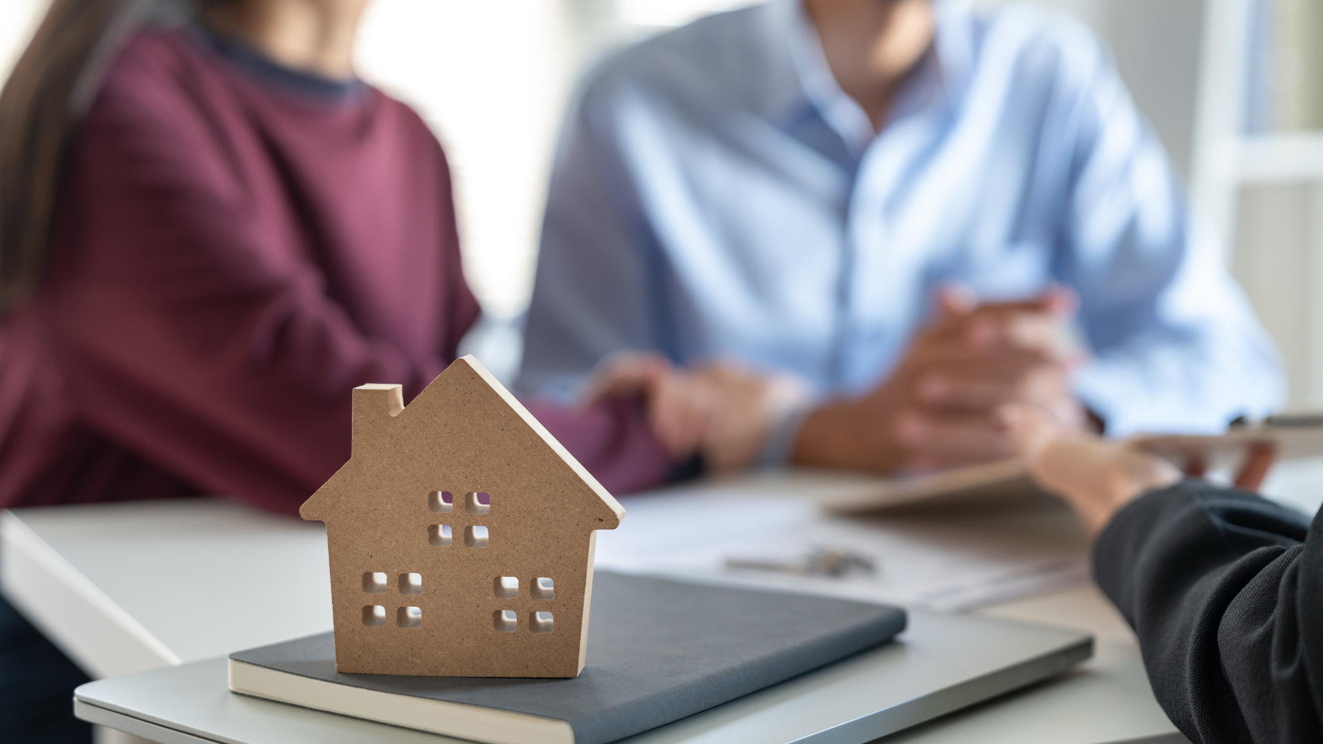A couple is sitting at a table with a model house on top of a book.