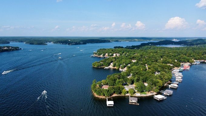 Aerial view of a large blue lake with numerous boats, surrounded by green islands and trees under a clear sky.
