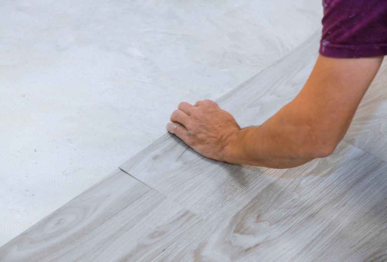 Person installing light gray laminate flooring on a white surface.