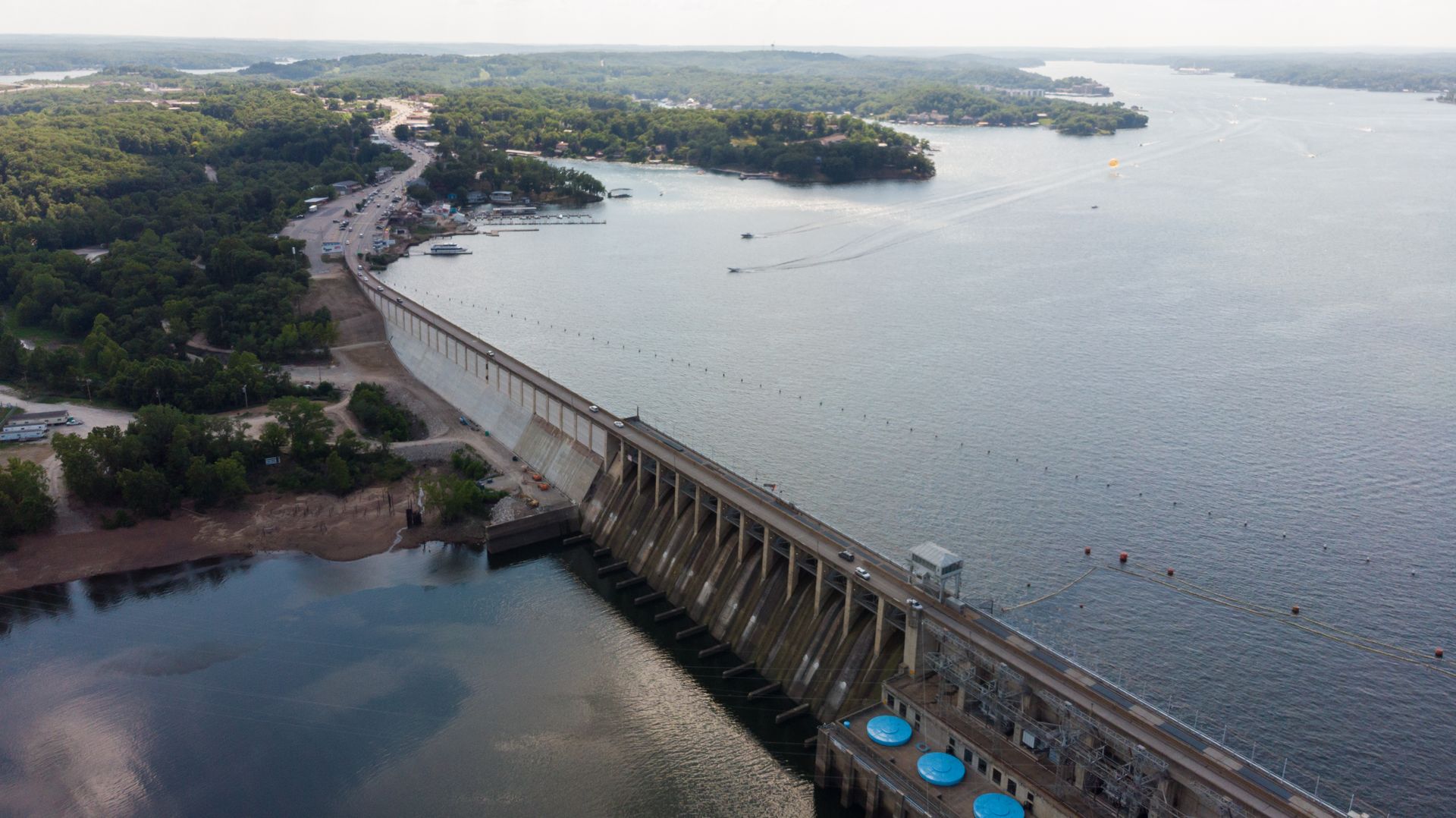 Aerial view of a dam on a body of water with a road and forested areas.