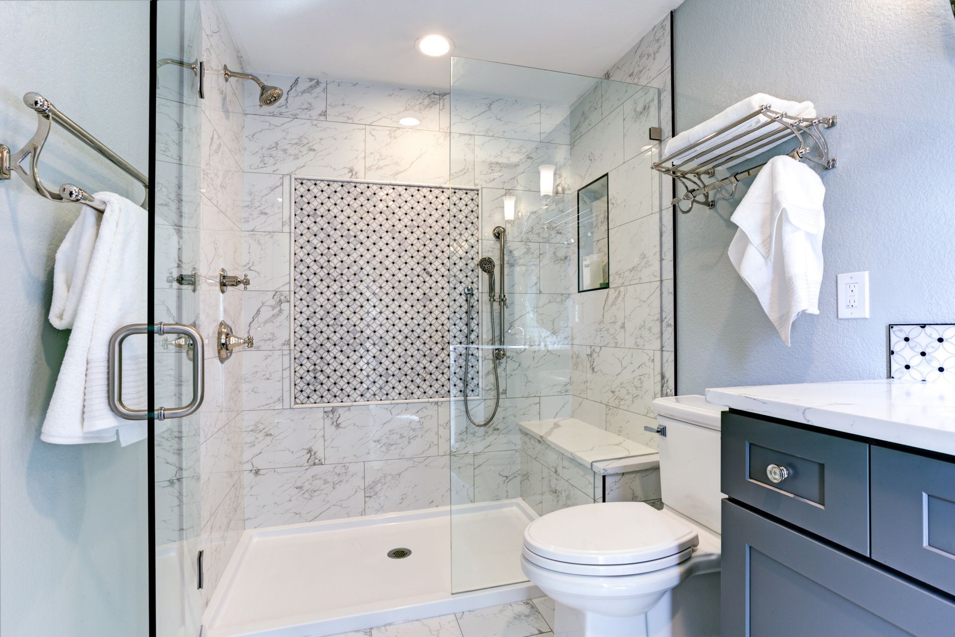 Modern bathroom with glass shower, white marble tile, gray vanity, and towel racks.
