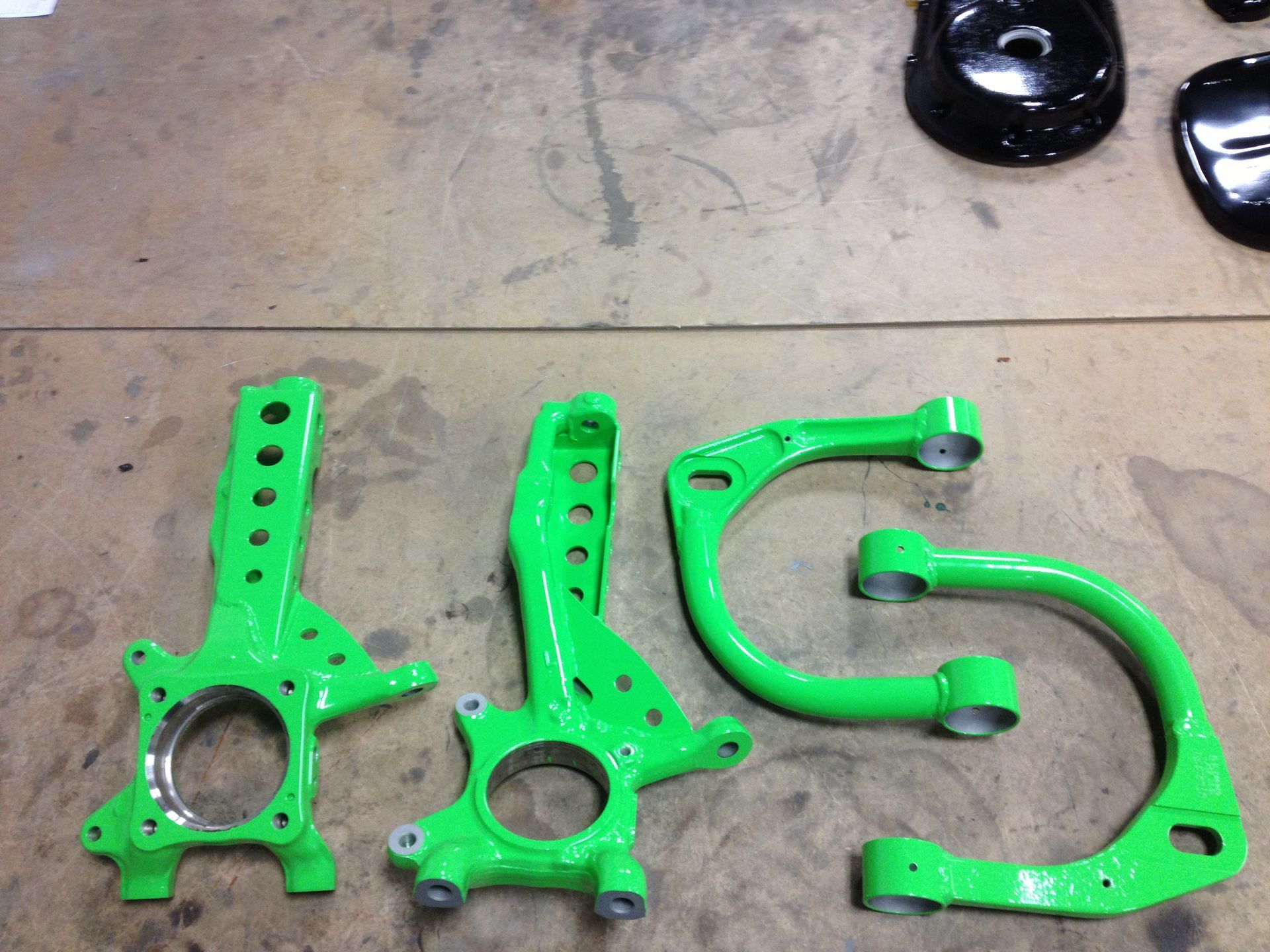 Bright green automotive suspension components on a wood surface.