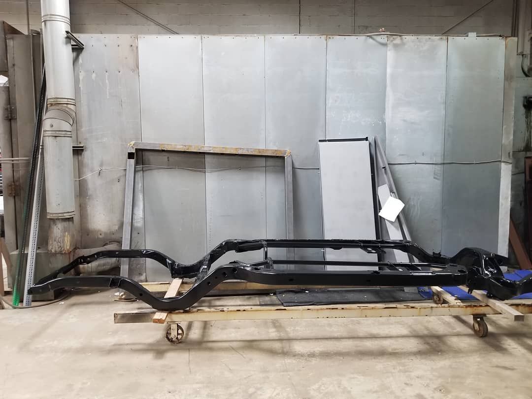 Black car frame on wooden supports in a grey workshop.