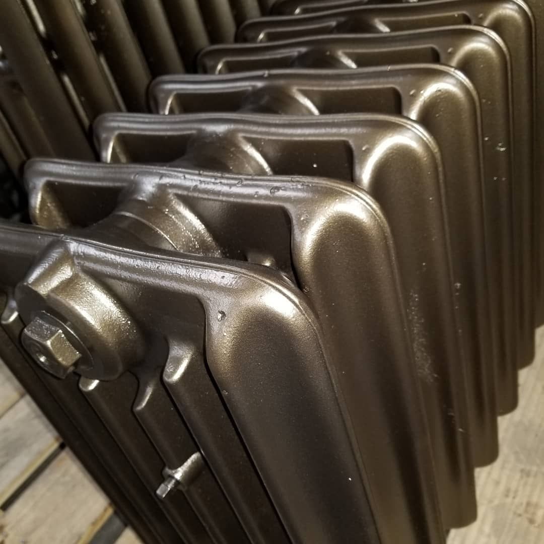 Close-up of rows of painted, dark-colored cast iron radiators.