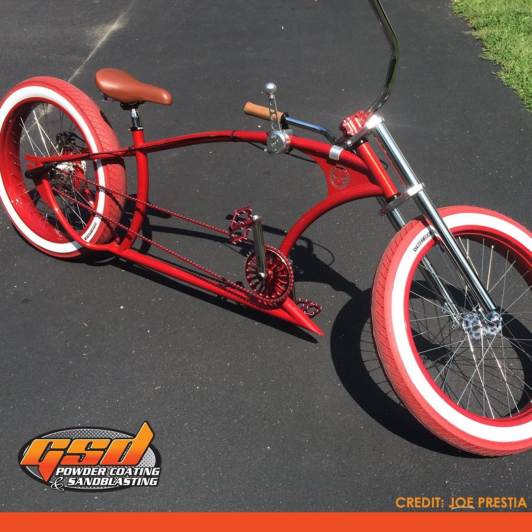 Red custom bicycle with white-walled tires, brown seat, on a paved surface.