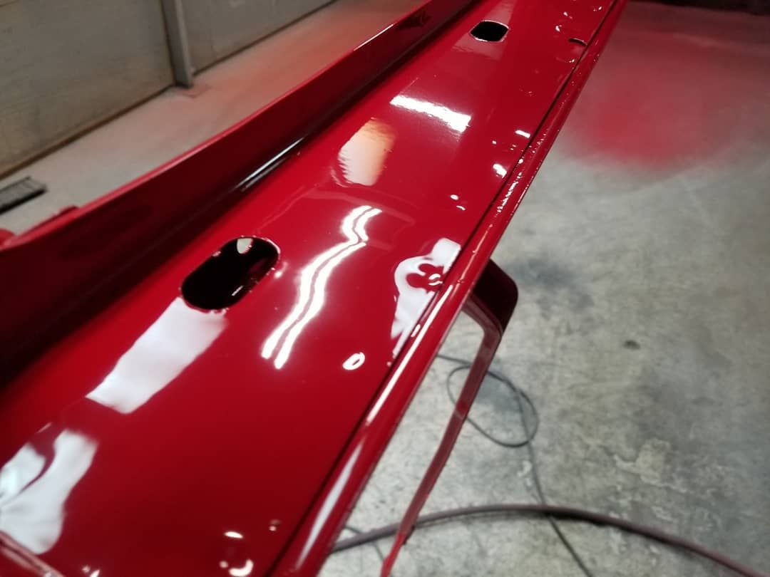 Red painted metal panel with visible reflections and oval cutouts, resting on a stand.