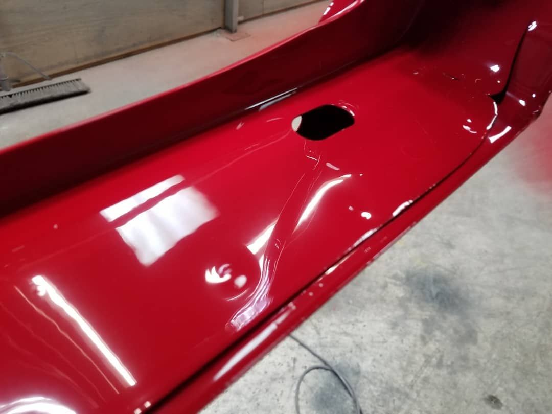Red car bumper, painted, with a visible dent and hole.