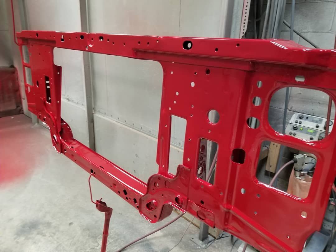Red painted metal vehicle frame in a spray booth.