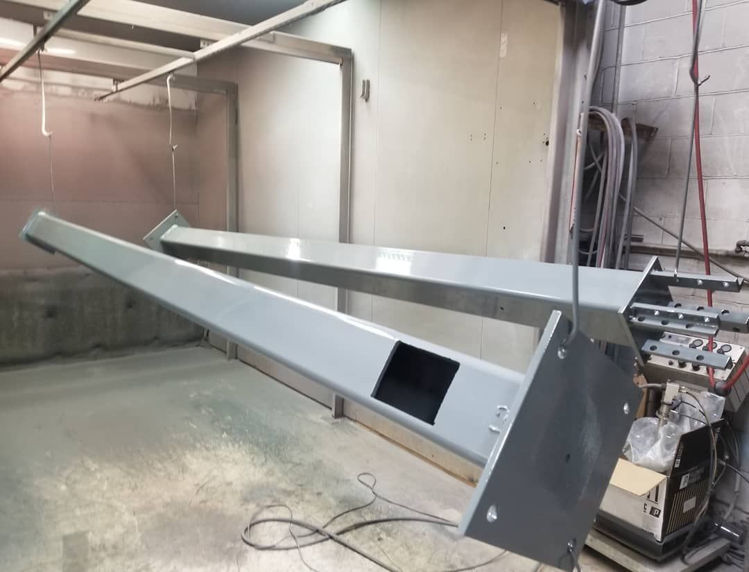 Two gray metal structures being powder coated in a spray booth.