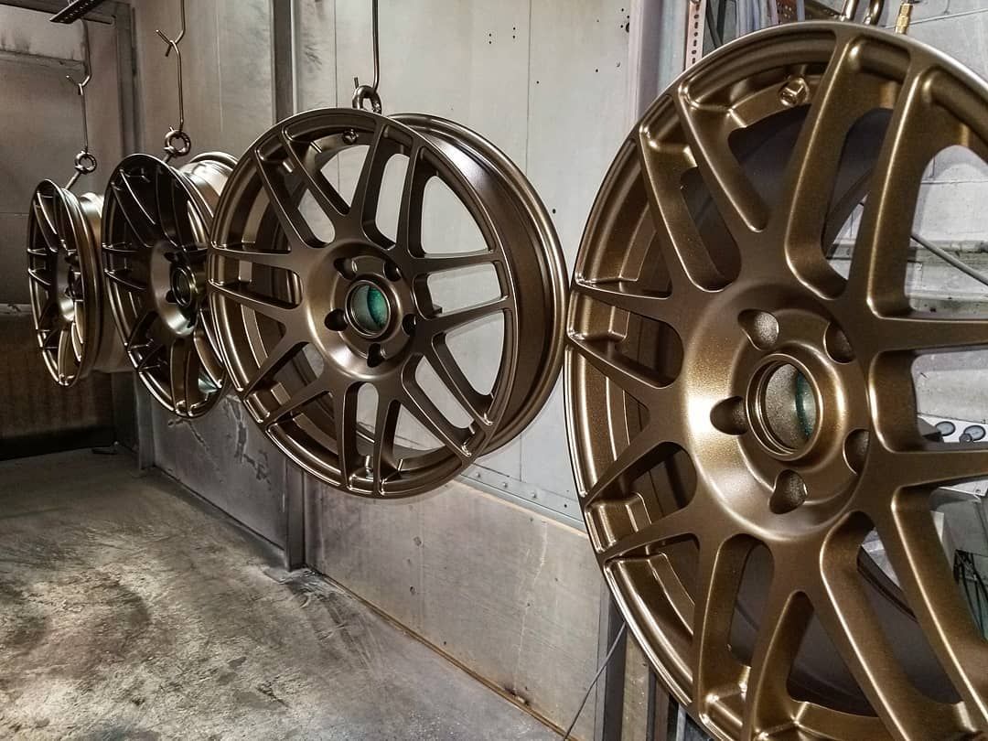 Four gold-painted car rims hanging in a workshop, ready for assembly.