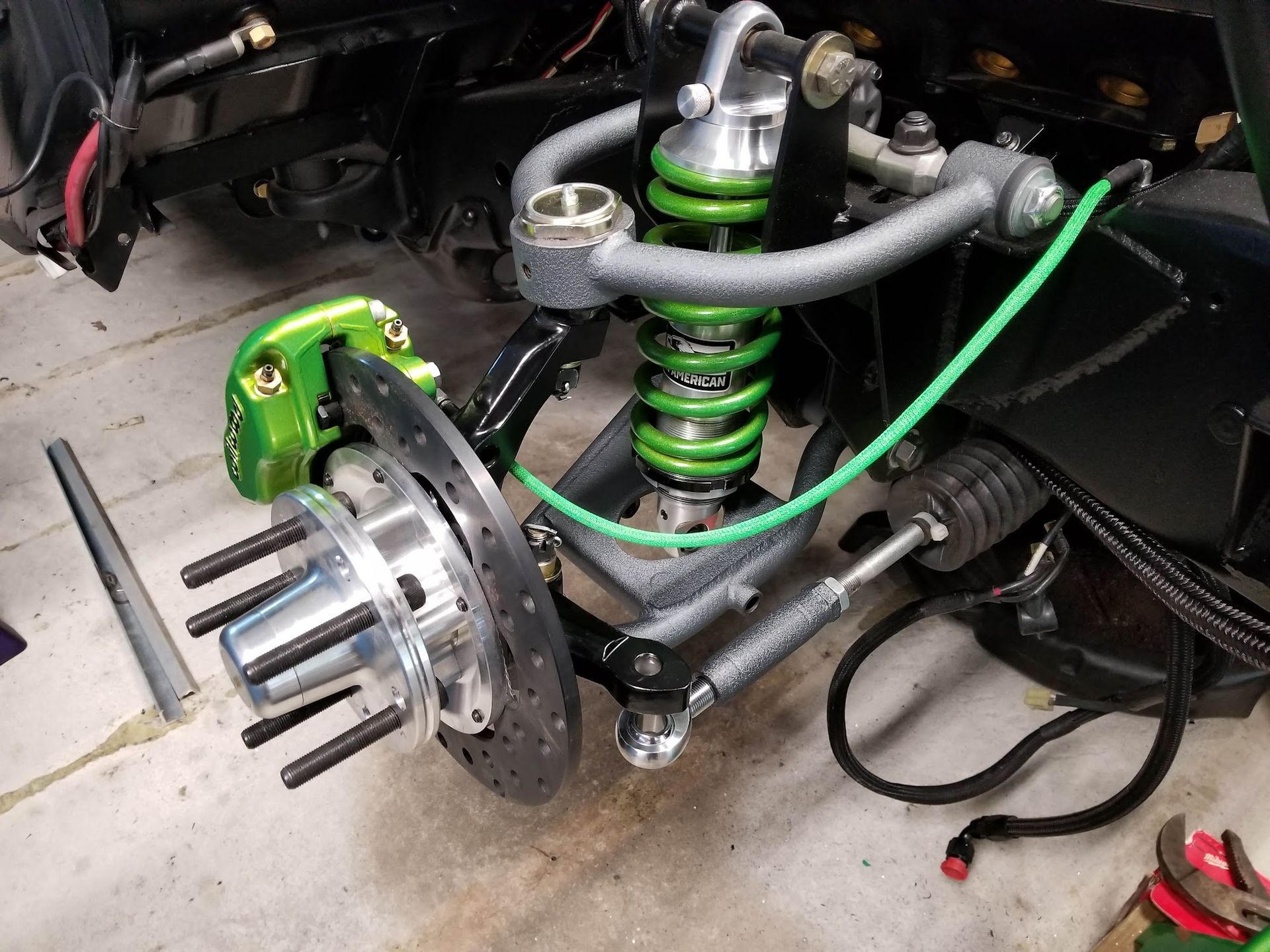 Green suspension and brake components of a vehicle, in a workshop setting.