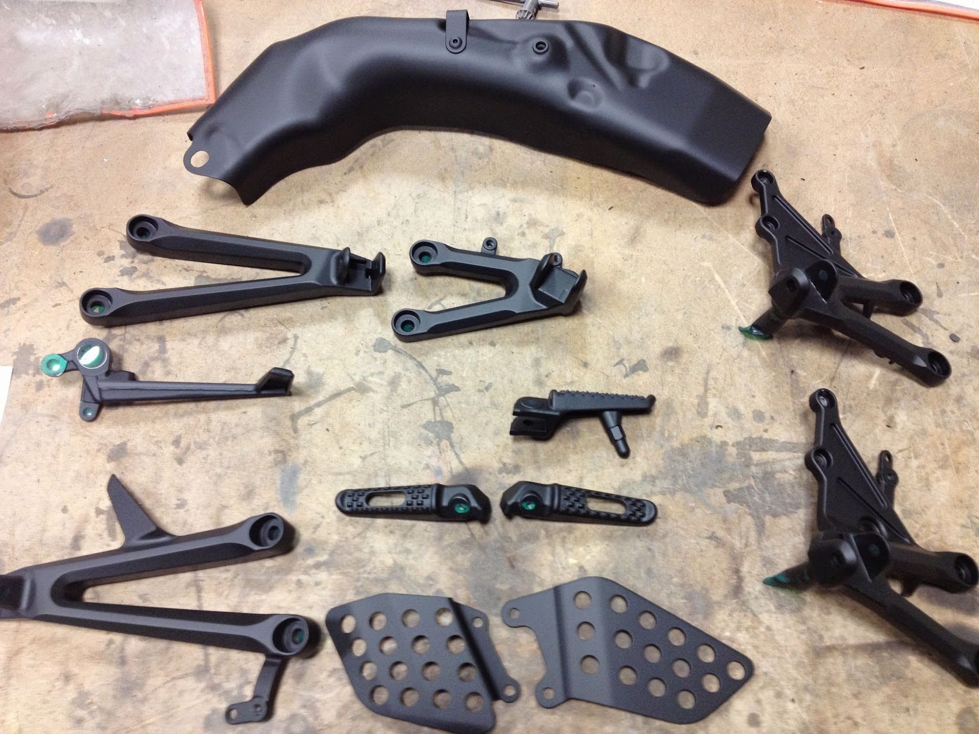 Black motorcycle parts laid out on a surface, including a fender, foot pegs, and suspension components.
