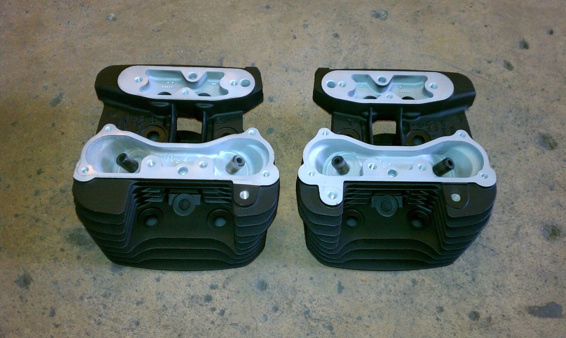 Two black motorcycle engine cylinder heads, viewed from the top with silver valve openings.