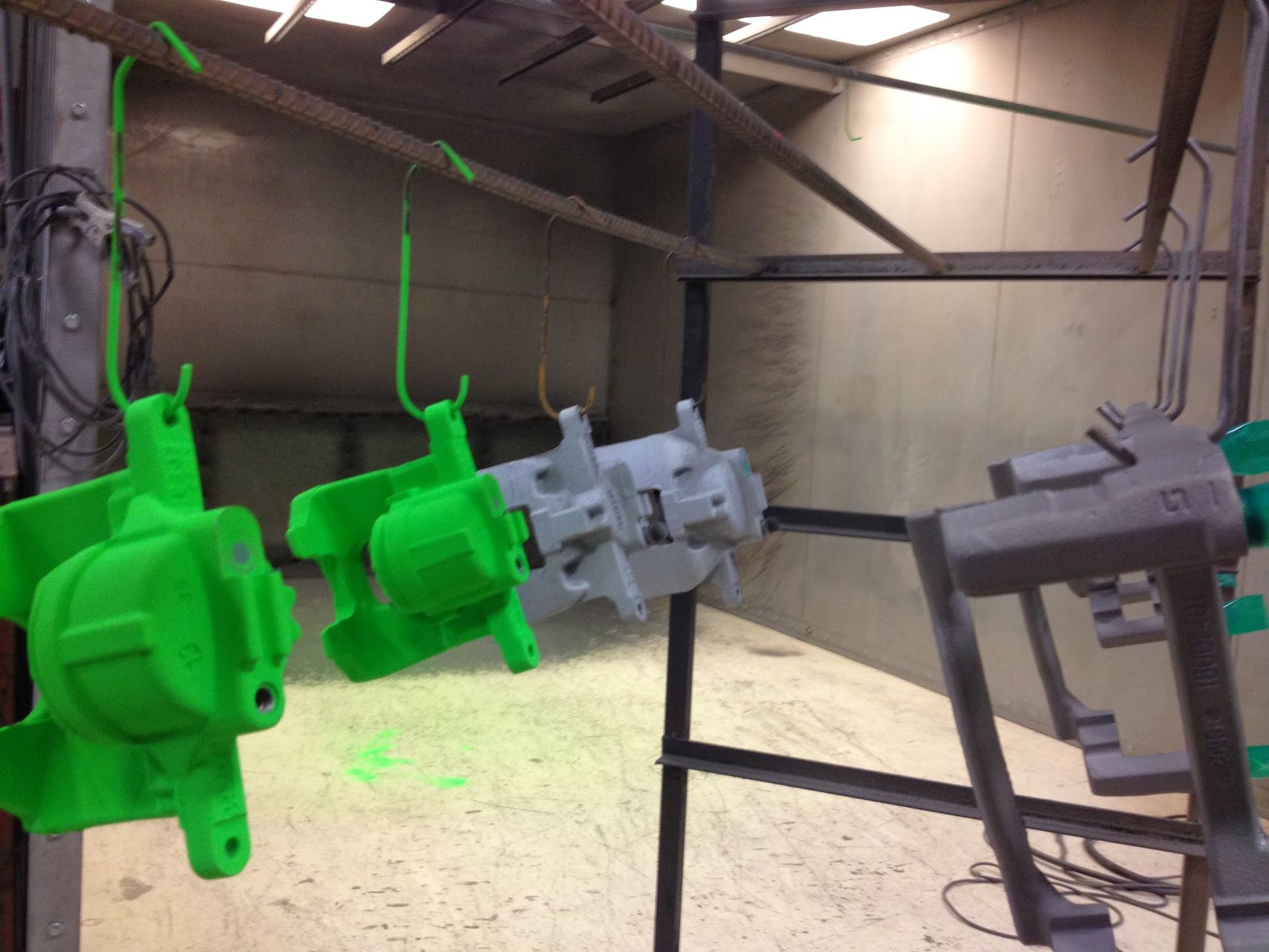 Green and gray painted machine parts hanging on a conveyor in an industrial setting.