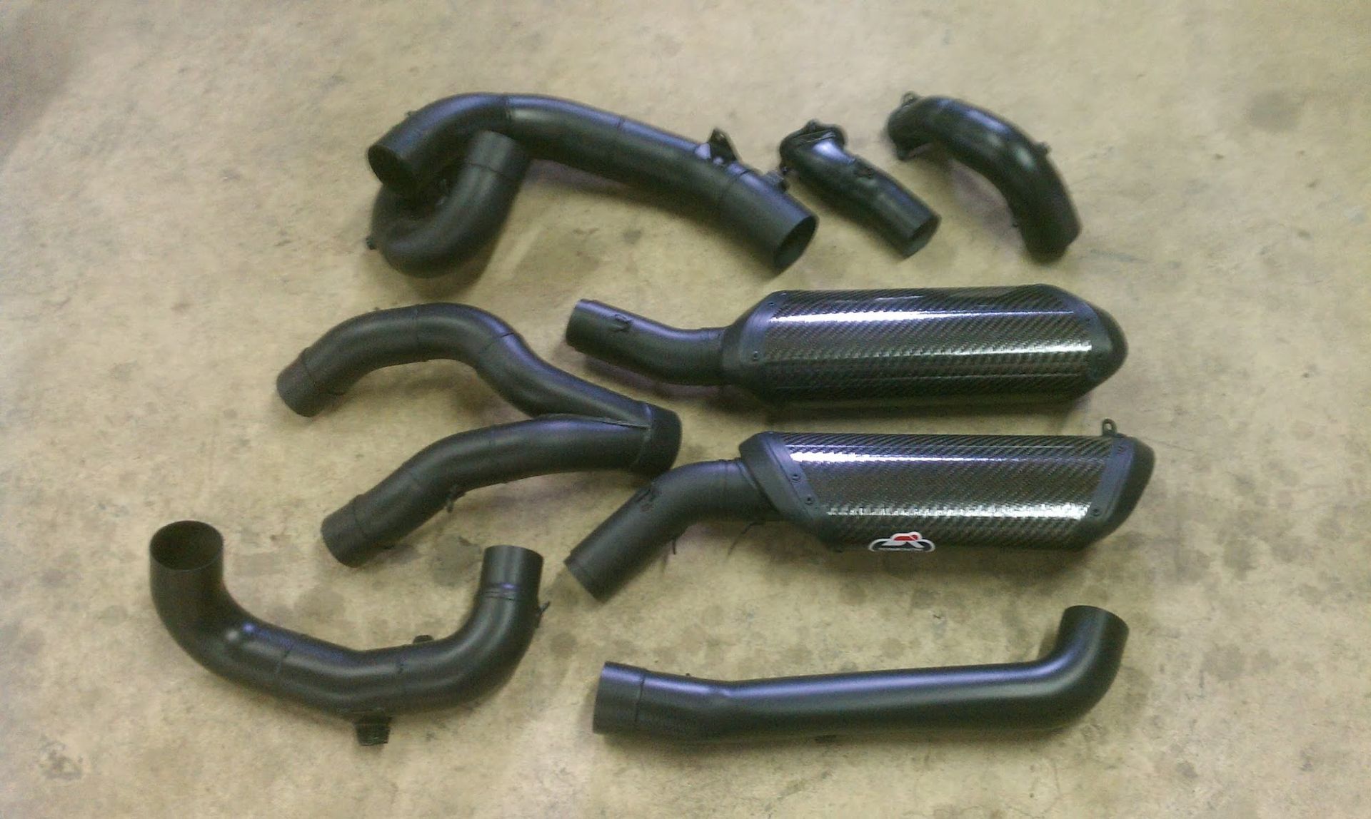 Black automotive air intake components and exhaust parts laid out on a surface.