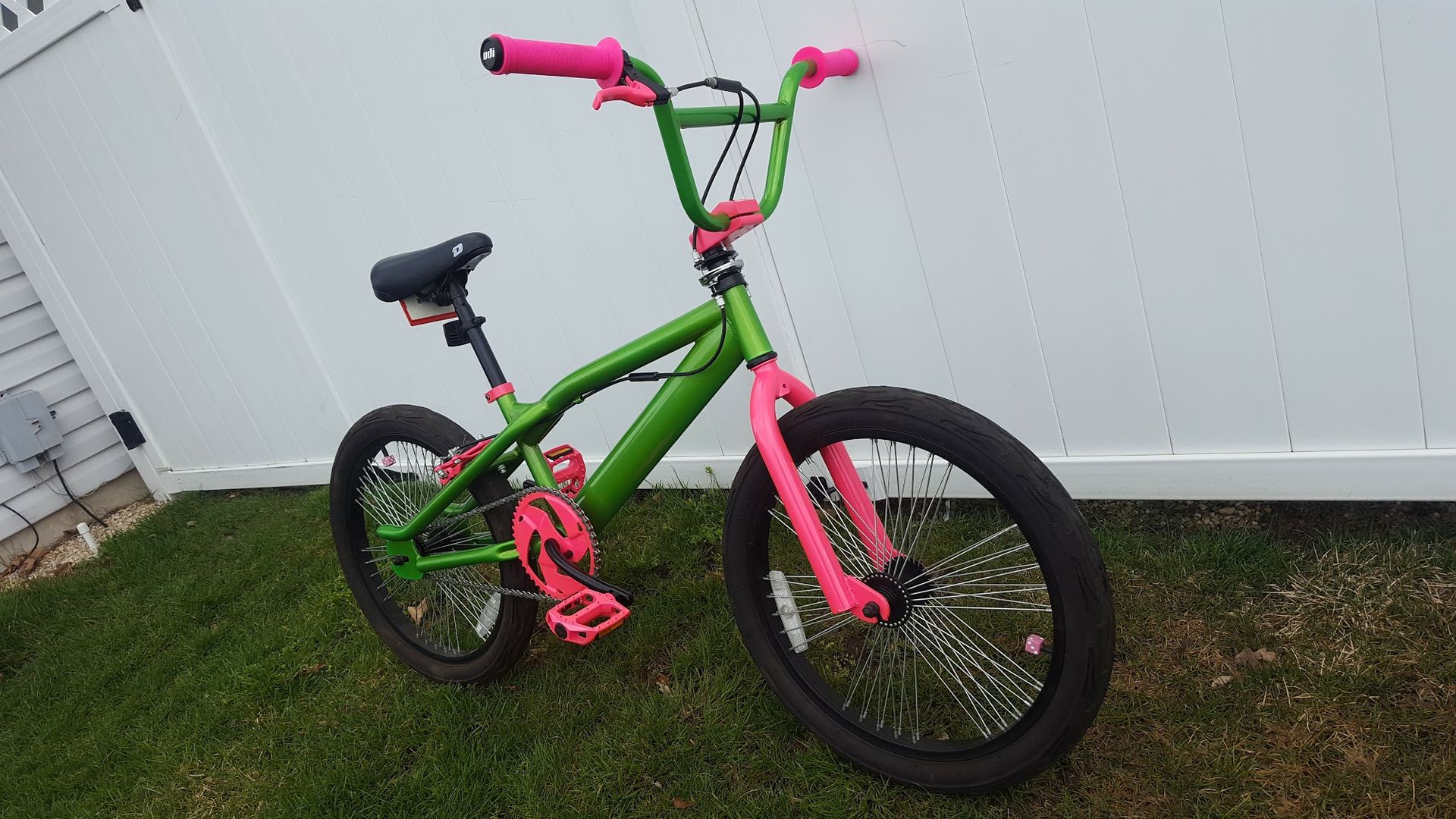 Green and pink BMX bike on grass, leaning against a white fence.