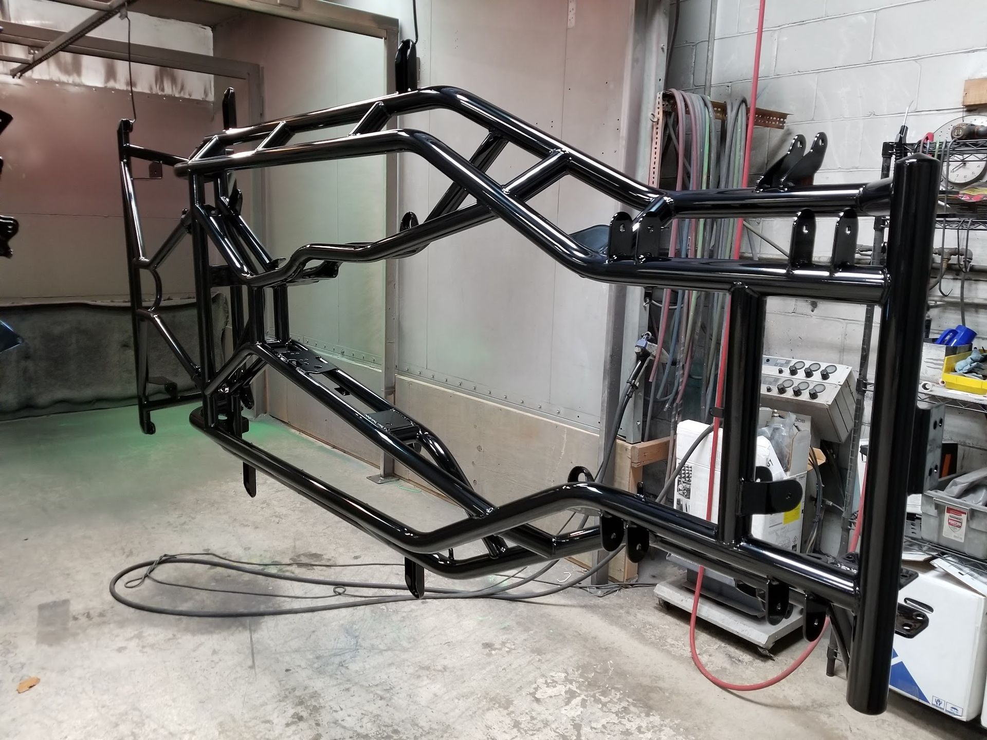 Black powder-coated off-road vehicle frame suspended in a workshop.