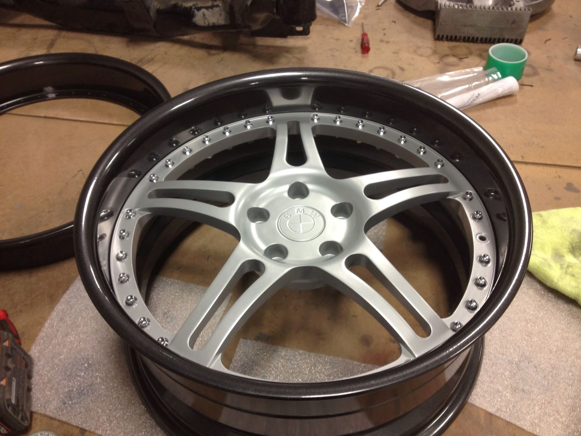 Silver and black car wheel rim with five spokes, assembled on a workbench.