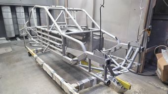 Metal parts in various colors, hanging on racks in a workshop, likely for painting or coating process.