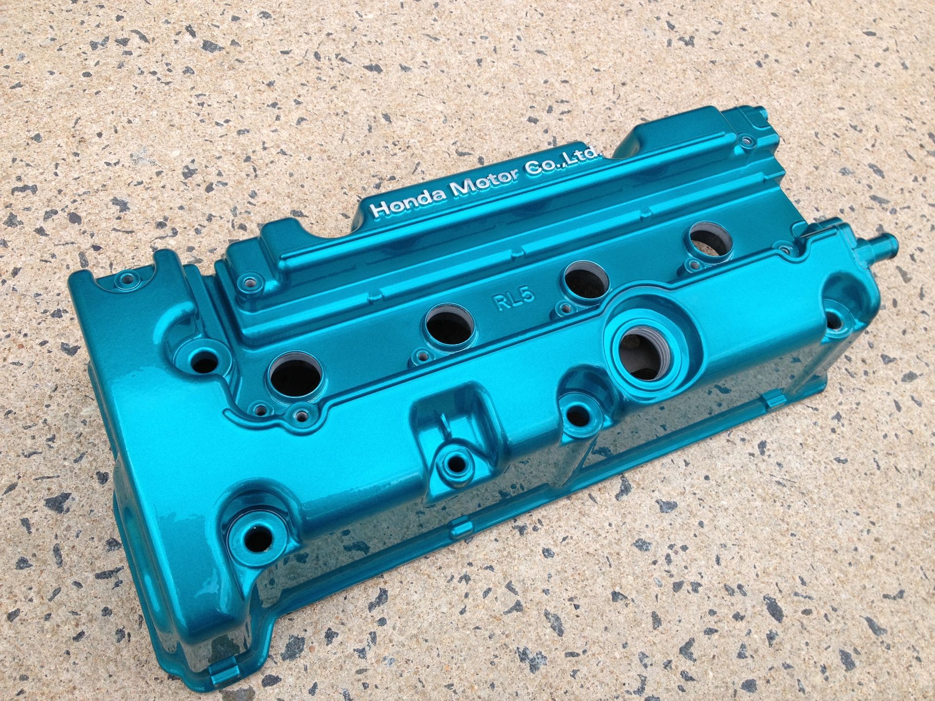 Blue-green painted engine valve cover on a concrete surface with the text 