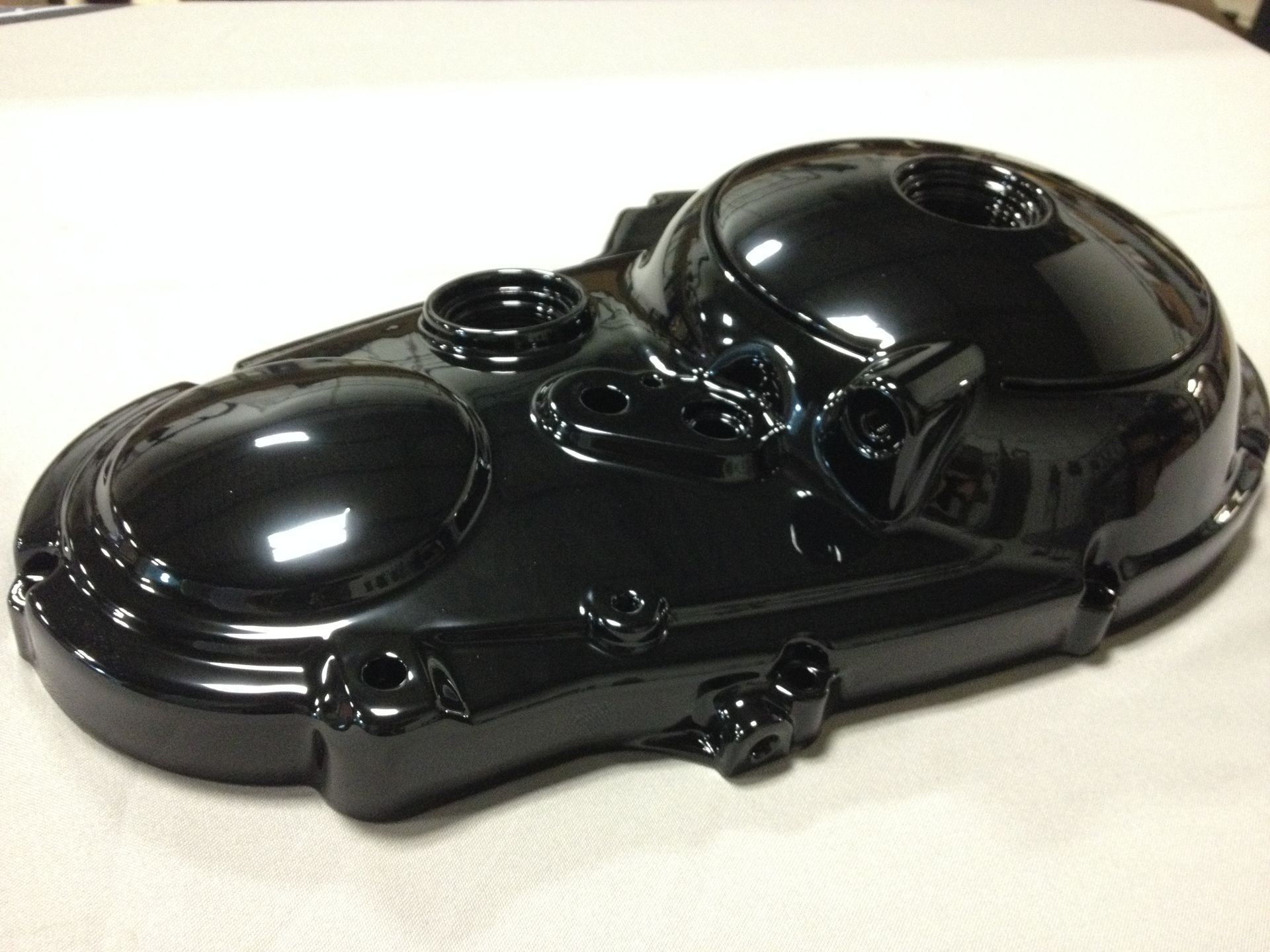 Black, glossy motorcycle engine cover with several circular and cylindrical openings.