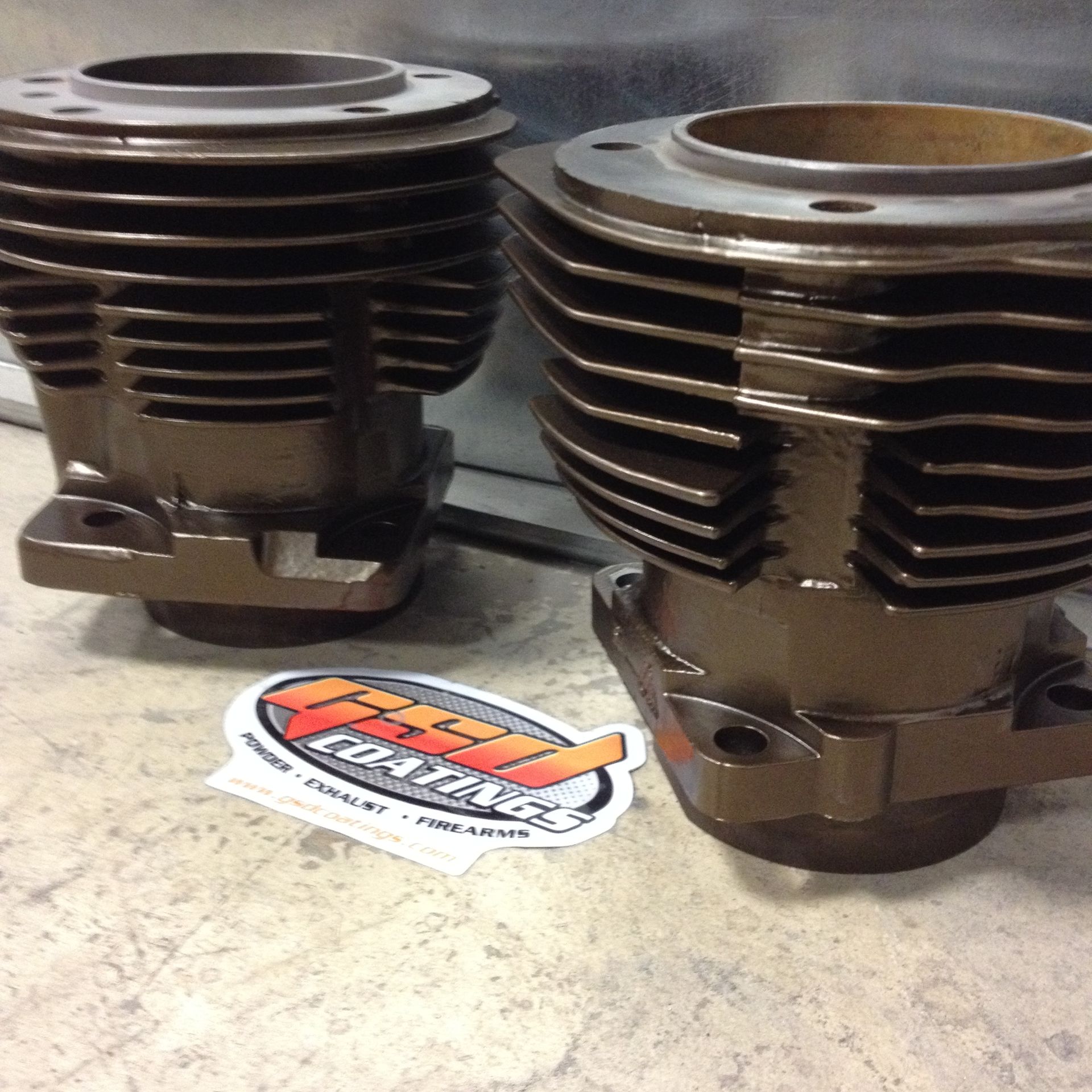 Two motorcycle cylinders painted brown, on a concrete surface with a sticker.