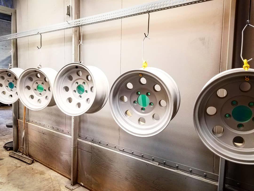 Five light-gray vehicle wheels hanging inside an industrial-style painting booth.
