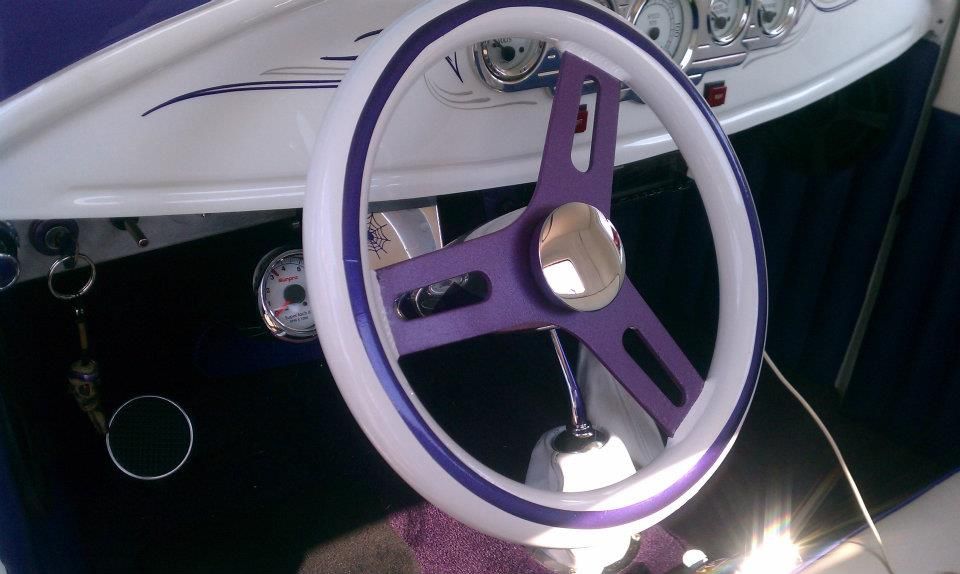 Purple and white steering wheel in a classic car, with a chrome hub and dashboard details.