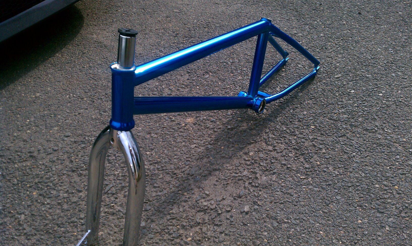 Blue BMX bike frame with silver fork on asphalt.