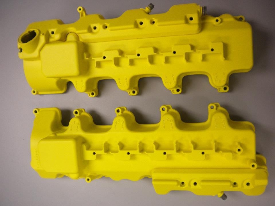Two bright yellow engine valve covers on a gray surface.