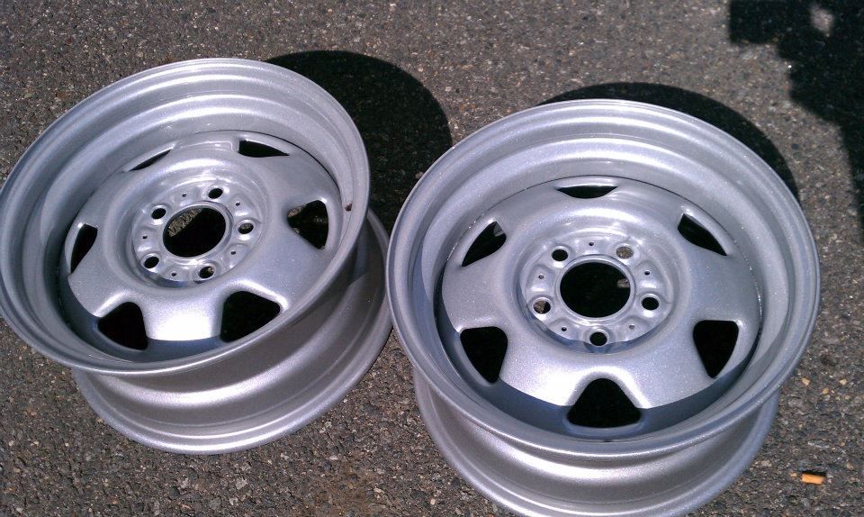 Two silver steel car wheels on asphalt, ready for tires.